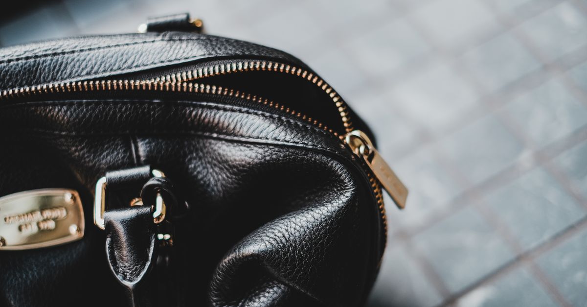 Close-up of a stylish black leather bag featuring a zipper and metal tag.